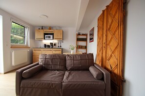 A living room with a sofa, a kitchen area with wooden cabinets, a window, and a wooden door. - Neues Appartement im Lepels Hof (Luetow)