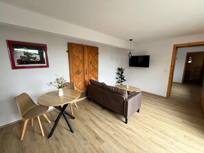A modern living room with a round wooden table, two chairs, a sofa, a TV mounted on the wall, and a wooden wardrobe. - Neues Appartement im Lepels Hof (Luetow)