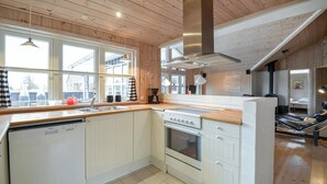 A kitchen with wooden cabinets, a stove, a dishwasher, and a large window. - Large holiday home close to the beach (Ebeltoft)