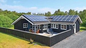A two-story building with solar panels on the roof, a covered patio with seating, and a fenced garden area. - Large holiday home close to the beach (Ebeltoft)