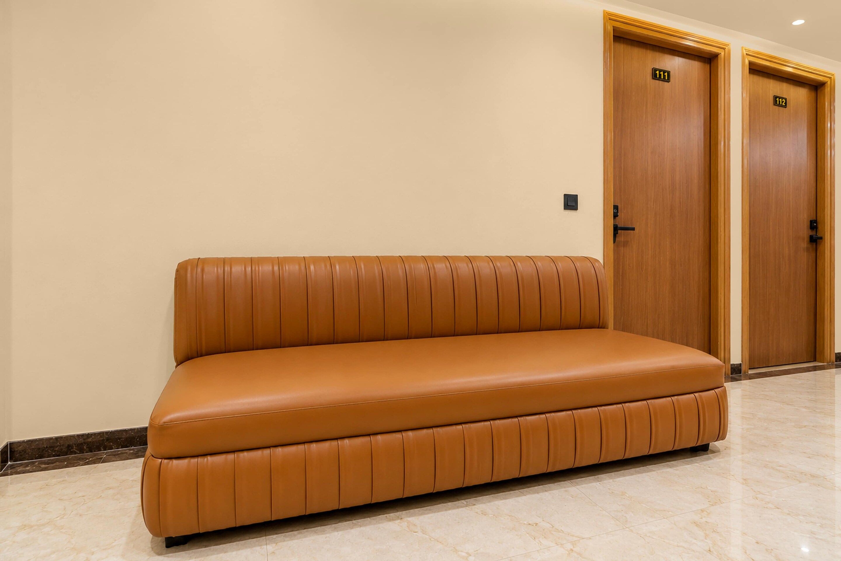 A tan leather sofa in a hallway with two wooden doors labeled 111 and 112.