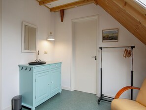 A room with a light blue cabinet, a mirror, a sink, a door, a coat rack, and a chair. - Cozy Vacation Rental in a Farmhouse (Callantsoog)