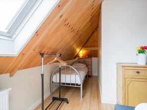 A dorm-style room with a skylight, a bed, a dresser, and a small table with a lamp. - Cozy Vacation Rental in a Farmhouse (Callantsoog)
