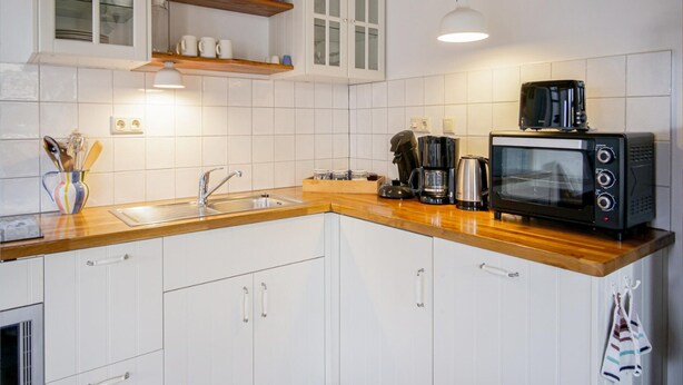 A kitchen with white cabinets, a wooden countertop, a coffee maker, a toaster, and a hanging light fixture. - Cozy Vacation Rental in a Former Farmhouse, Surrounded by Nature (Callantsoog)