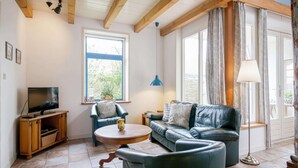 A living room with a television, a sofa, a chair, a coffee table, and a lamp. - Cozy Vacation Rental in a Former Farmhouse, Surrounded by Nature (Callantsoog)