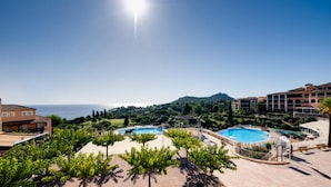 Ein Resort mit zwei Swimmingpools, Blick auf das Meer und einer hügeligen Landschaft im Hintergrund.