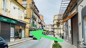 A narrow street with buildings on either side, a parked car, and a green arrow pointing down the street. - Charming 2-bedroom apartment with AC in Vibo Valentia (Vibo Valentia)
