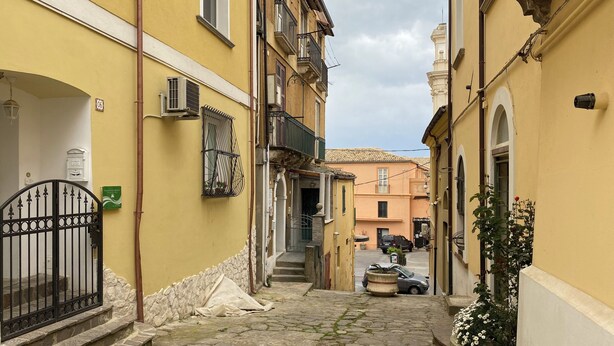 A narrow cobblestone street between yellow buildings with a gate, a staircase, and a parked car. - Charming 2-bedroom apartment with AC in Vibo Valentia (Vibo Valentia)