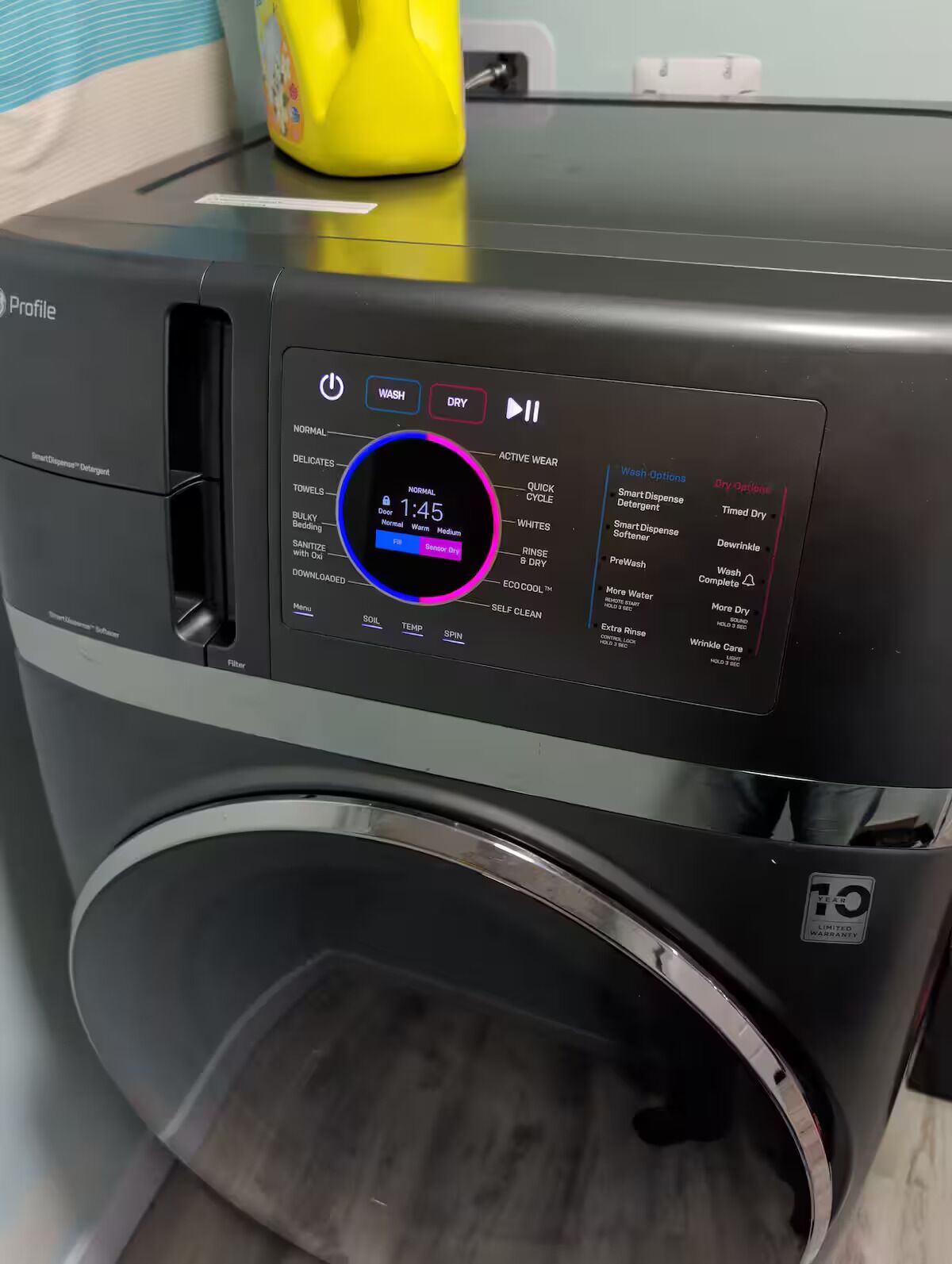A front view of a modern, compact washer with a digital control panel displaying various wash options and settings.