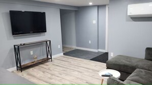 A living room with a flat-screen TV, grey sofa, and a small side table. - Salt and Spruce private 1 bedroom suite with double bed, kitchen, and laundry (Mount Pearl)