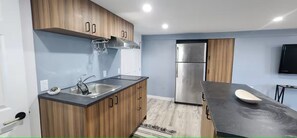 A modern kitchen with wooden cabinets, a stainless steel refrigerator, and a black countertop. - Salt and Spruce private 1 bedroom suite with double bed, kitchen, and laundry (Mount Pearl)