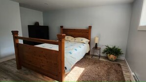 A bedroom with a wooden four-poster bed, a small bedside table with a lamp, a potted plant, and a radiator. - Salt and Spruce private 1 bedroom suite with double bed, kitchen, and laundry (Mount Pearl)