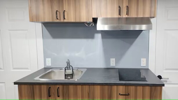 A kitchen with wooden cabinets, a stainless steel sink, and a modern stove. - Salt and Spruce private 1 bedroom suite with double bed, kitchen, and laundry (Mount Pearl)