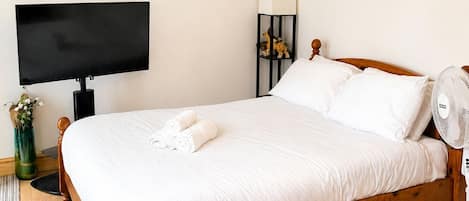 A neatly made bed with white linens, a flat-screen TV on a stand, a lamp, and a decorative piece on the wall.
