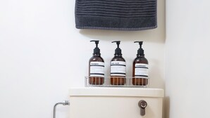 Een badkamer met een toilet, een wastafel en drie flessen toiletartikelen op een plank boven het toilet.