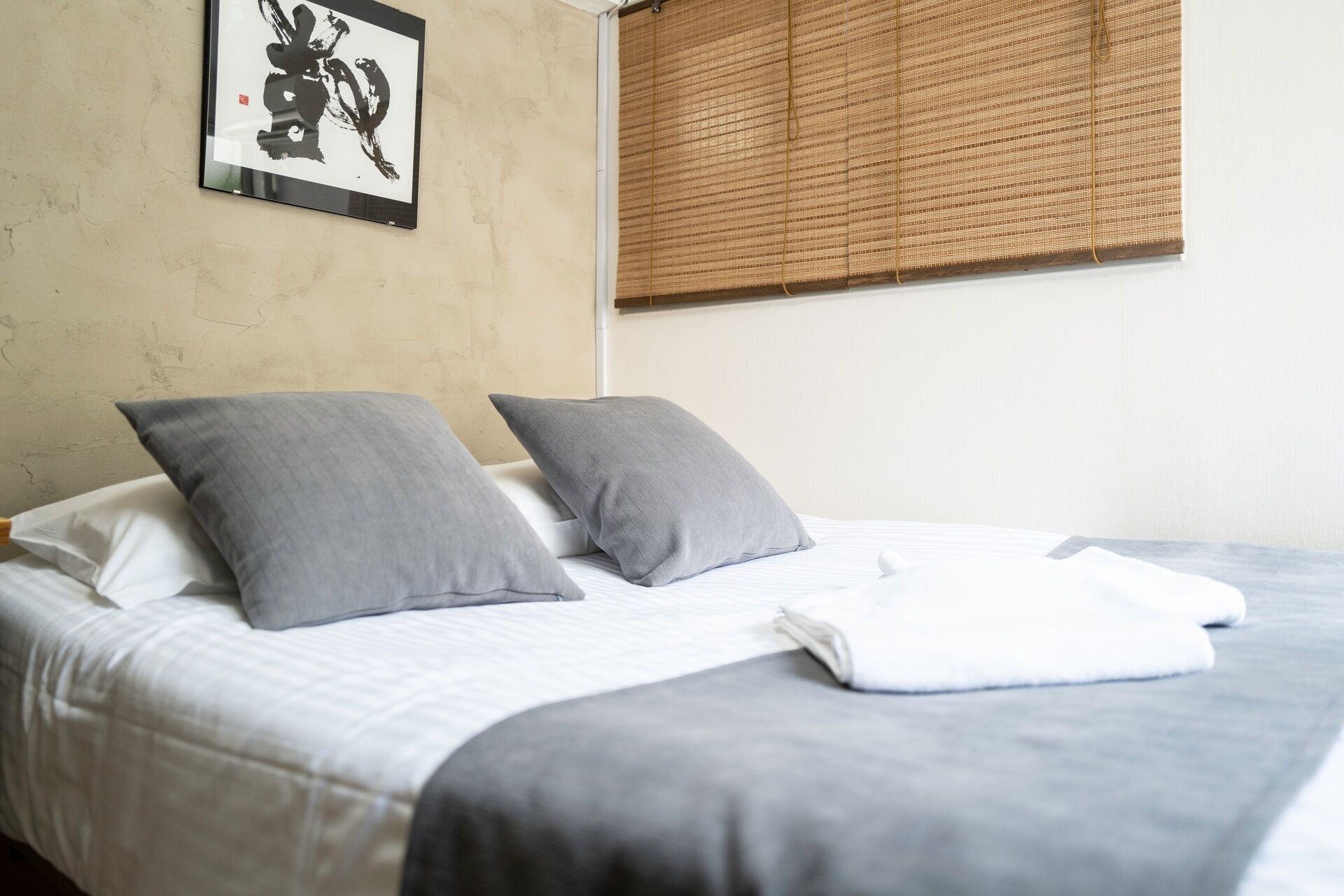 Ein Bett mit zwei Kissen, einer weißen Decke und einem gerahmten Bild an der Wand.
