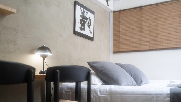 Een kamer met een bed, twee stoelen, een bureau, een lamp en een lijst aan de muur.