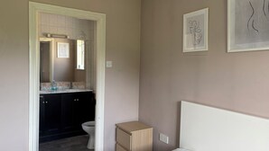Un baño con inodoro, lavamanos y armario. Hay un espejo sobre el lavamanos y un pequeño mueble junto al inodoro.