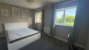 Un dormitorio con cama, un radiador, una ventana con cortinas y cuadros en la pared.