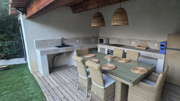 Una cucina esterna con tavolo, sedie, lavello incassato, forno a microonde e frigorifero.