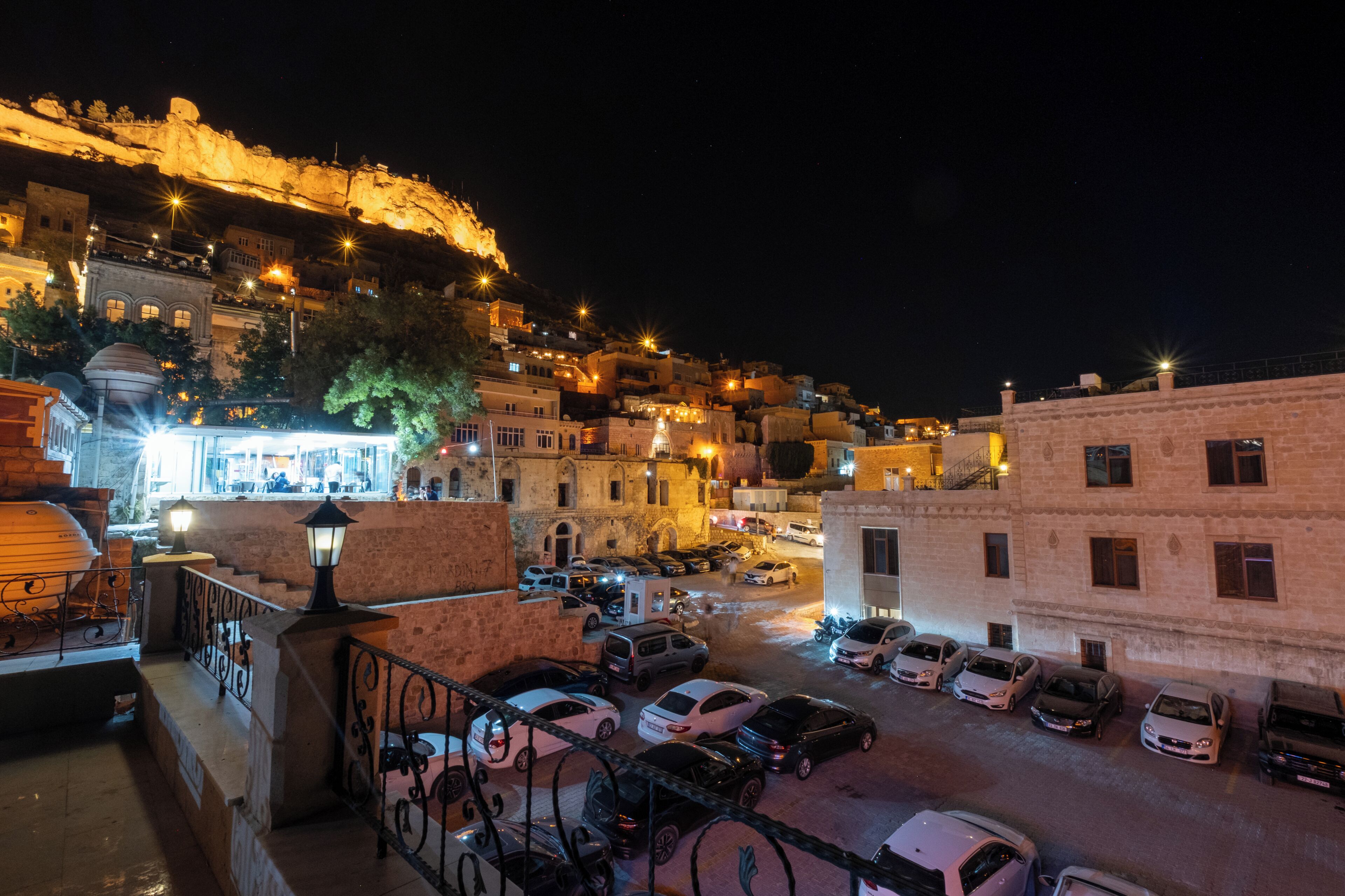 Vista nocturna de un pueblo histórico con una colina destacada, edificios iluminados y un área de estacionamiento.