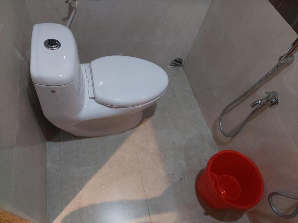 Un inodoro blanco, un balde rojo y una manguera de ducha en un baño.
