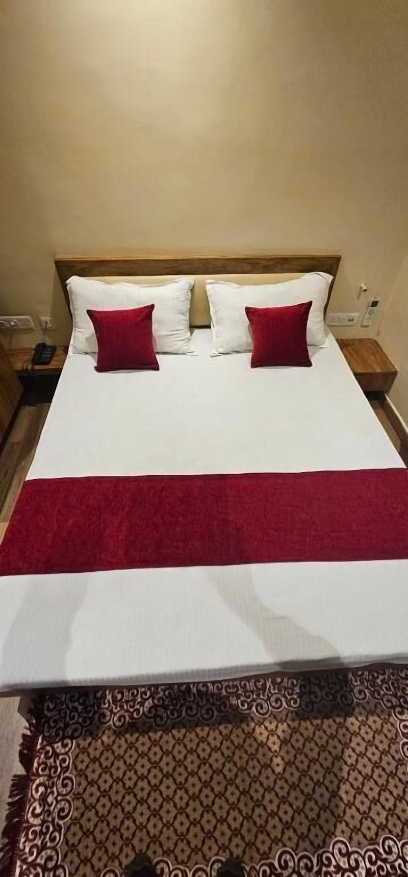 A bed with white linens, two red pillows, a red runner, and a patterned rug.