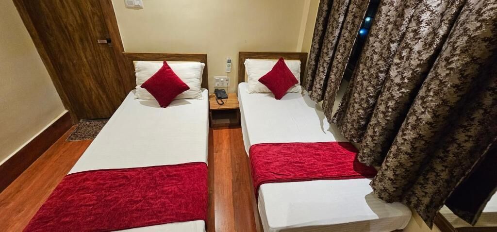 A room with two beds, each with white bedding and red accents, a wooden floor, and a curtain with a floral pattern.