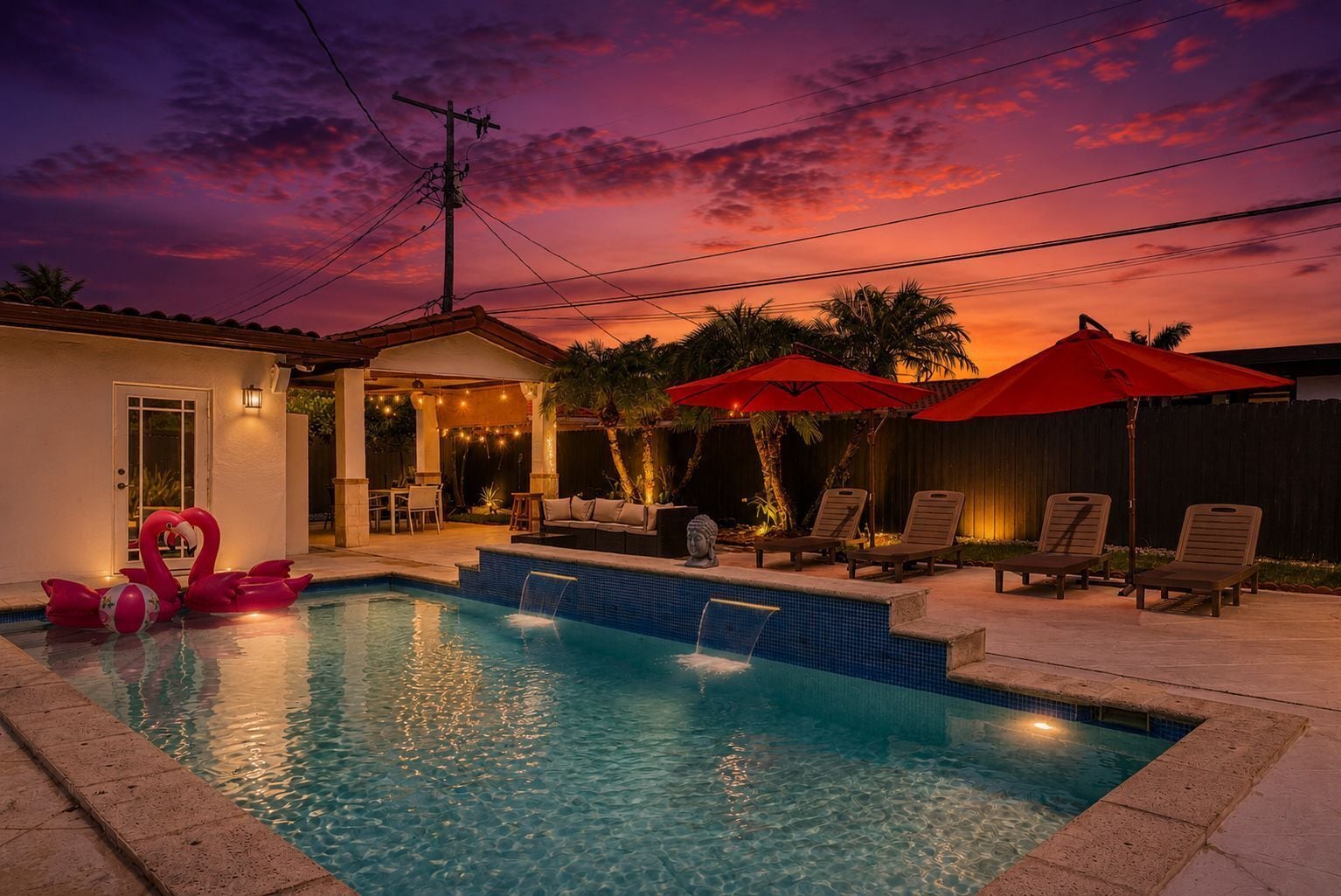 Ein Schwimmbecken mit Liegestühlen und Sonnenschirmen, ein kleines Haus mit einer Tür sowie ein Sonnenuntergangshimmel.