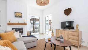 A modern living room with a sofa, TV, wooden cabinet, and a fireplace. - Casa Aurea V3 com Piscina Privada (Tavira)