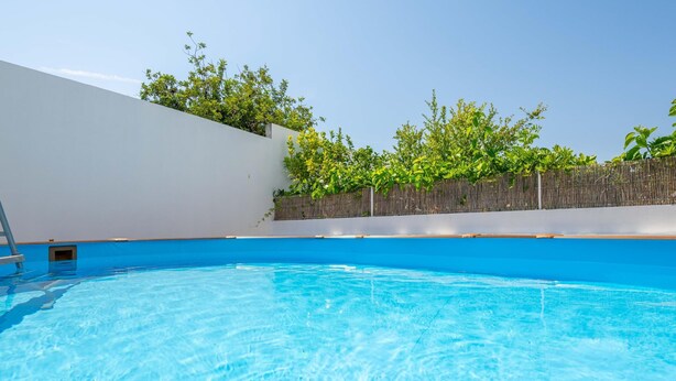 A clear blue swimming pool with a white wall and a wooden fence in the background. - Casa Aurea V3 com Piscina Privada (Tavira)