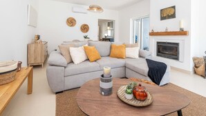 A modern living room with a grey sectional sofa, a round wooden coffee table, and a fireplace. - Casa Aurea V3 com Piscina Privada (Tavira)
