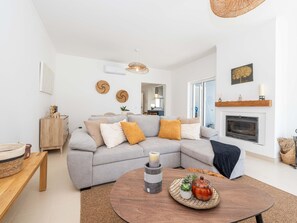Ein modernes Wohnzimmer mit einem grauen Ecksofa, einem runden Couchtisch aus Holz und einem Kamin.