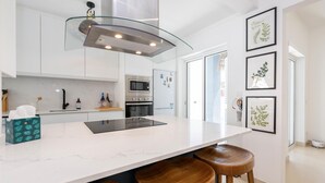 A modern kitchen with a central island, stainless steel appliances, and wooden stools. - Casa Aurea V3 com Piscina Privada (Tavira)