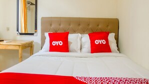 A bed with a tufted headboard, two pillows with 'OYO' branding, a wooden nightstand, a mirror, and a painting of tulips. - Luxury Deluxe DBL Retreat W/ Free Wifi and Parking (Jakarta)