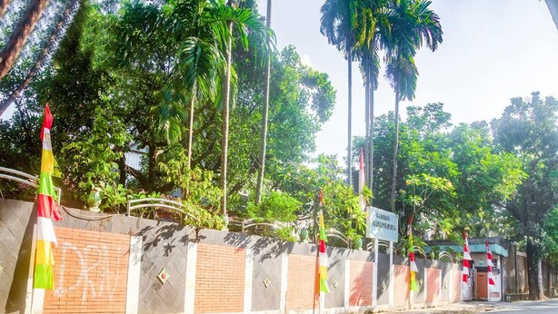 A road lined with a brick wall, palm trees, and a flagpole. - Luxury Deluxe DBL Retreat W/ Free Wifi and Parking (Jakarta)