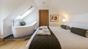 A bedroom with a large bed, a bathtub, and a skylight. - The Keep -  A Stunning One Bedroom Apartment (Kirknewton)