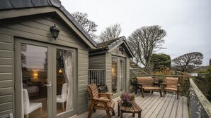 A wooden deck with outdoor seating, a glass door entrance, and a view of trees and a body of water. - The Keep -  A Stunning One Bedroom Apartment (Kirknewton)