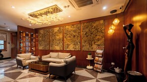 A lobby with a checkered floor, two sofas, a coffee table, a chandelier, a wall with a textured pattern, and a statue.