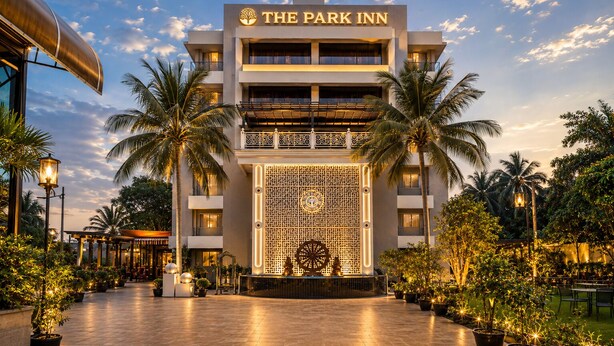 A hotel with a prominent sign reading 'The Park Inn,' featuring a modern architectural design with a decorative facade and palm trees surrounding the entrance.