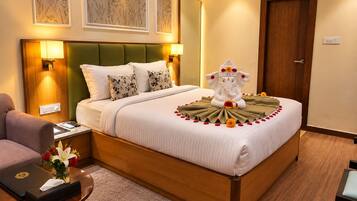 A hotel room with a bed, a green headboard, a wooden nightstand, a desk, and a chair.