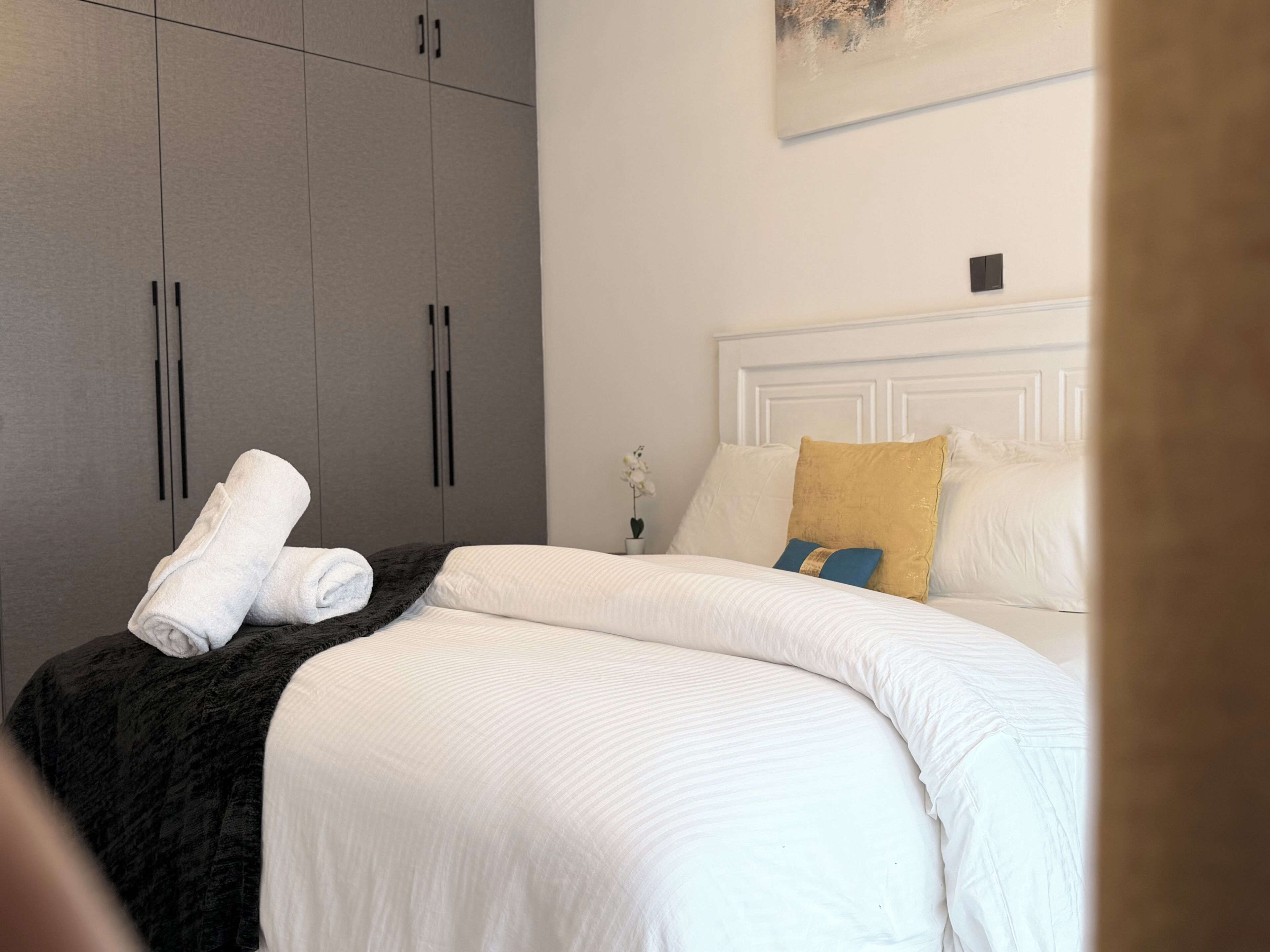 Un dormitorio con una cama, una mesita de noche, un cuadro y armarios grises.