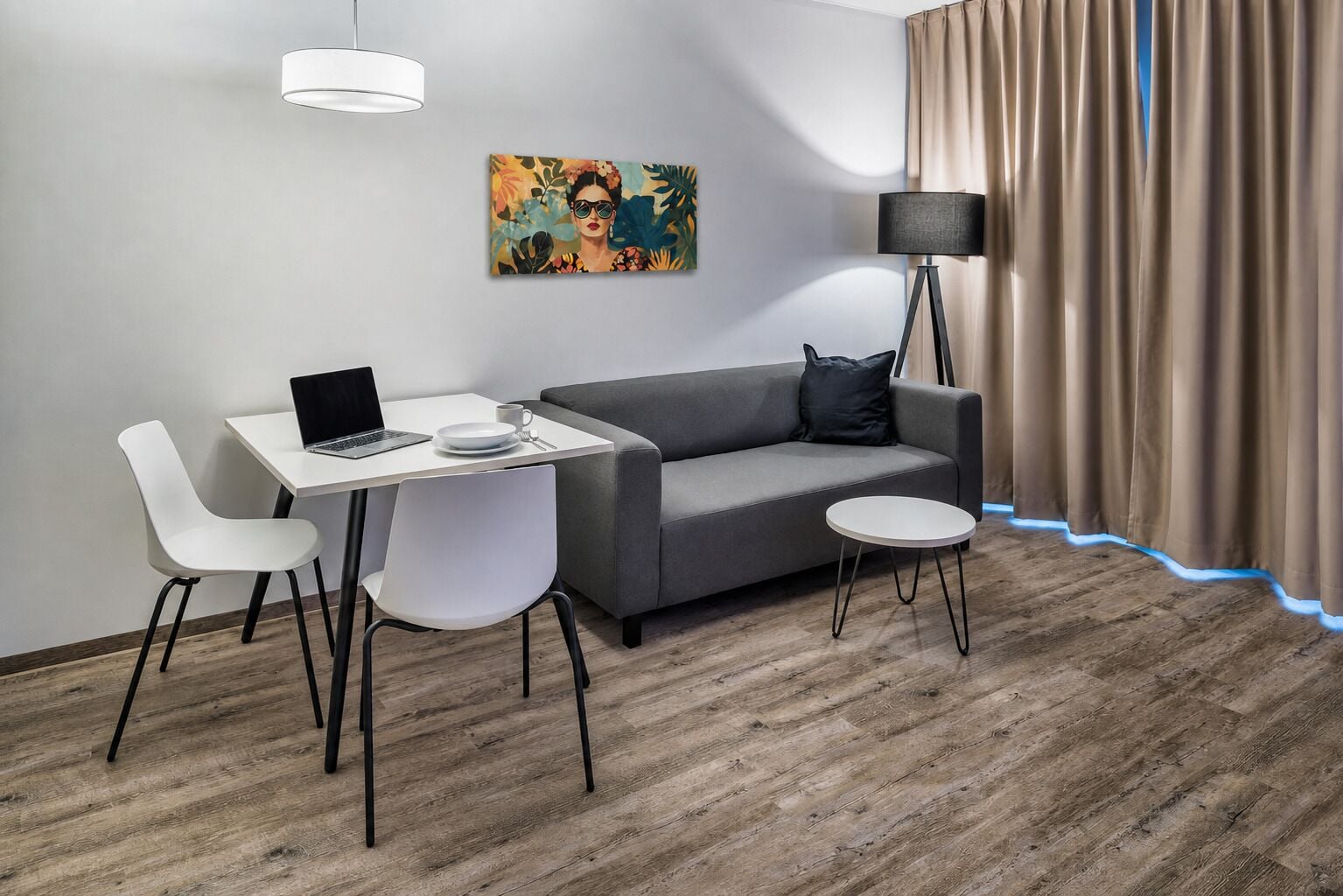 Een moderne kamer met een grijze bank, witte stoelen, een tafeltje, een laptop, een schilderij, een vloerlamp en een gordijn.