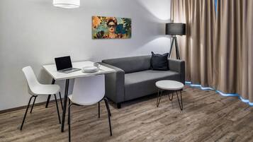 Een moderne kamer met een grijze bank, witte stoelen, een tafeltje, een laptop, een schilderij, een vloerlamp en een gordijn.