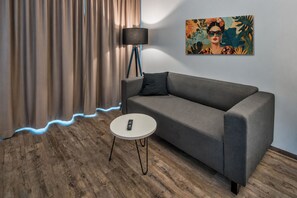 A modern room with a grey sofa, a round white coffee table, a floor lamp, and a painting on the wall.