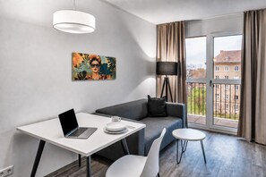 A modern living room with a sofa, a dining table, a laptop, and a painting on the wall. - MIILOX Apartments Dresden am Park (Dresden)