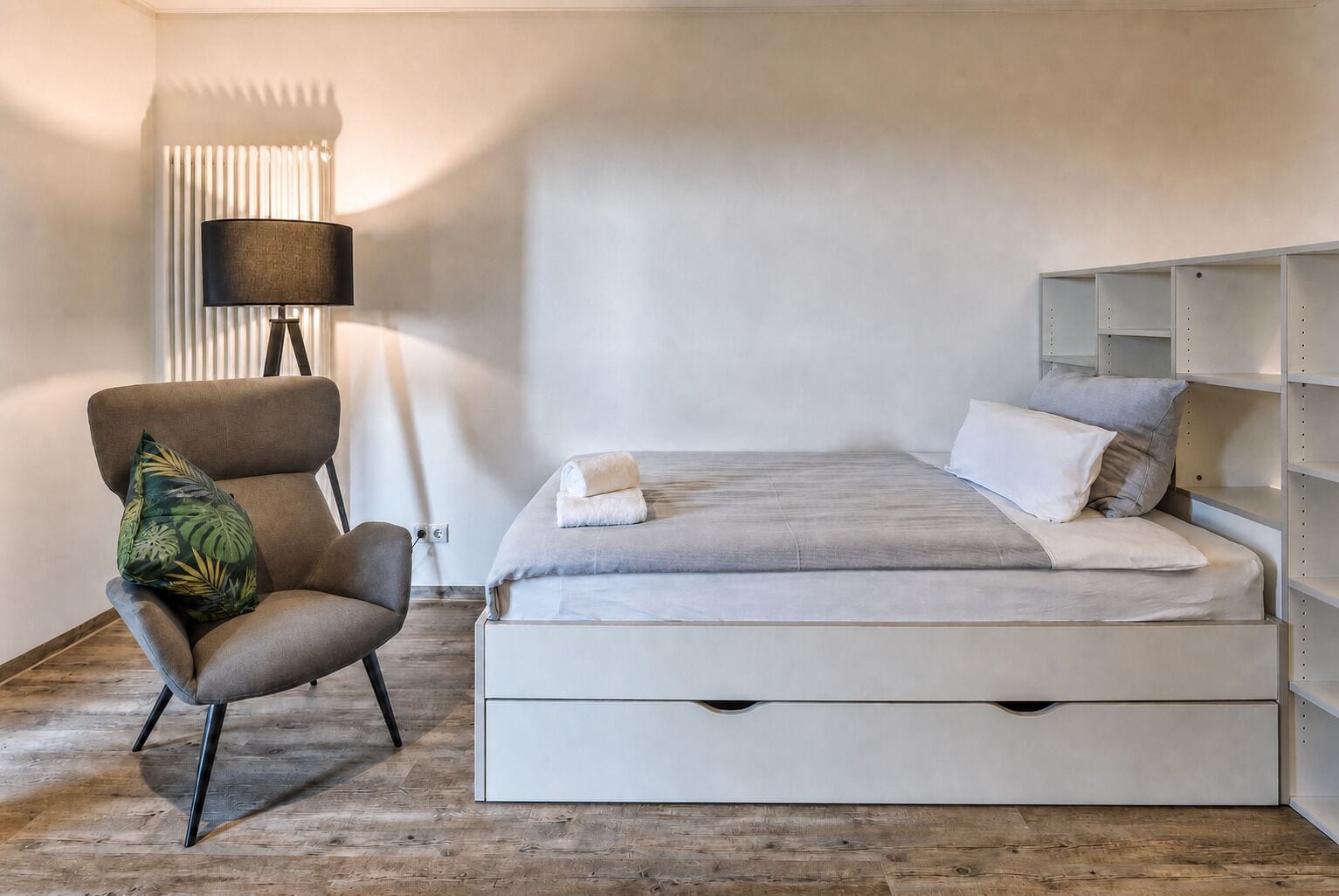 A bedroom with a bed, a chair, a lamp, and a shelving unit.