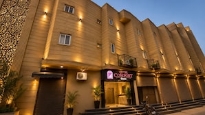 A hotel with a curved facade, multiple balconies, and a well-lit entrance. - Qotel Comfort Oasis Rajouri Garden (New Delhi)