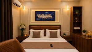 A hotel room with a large bed, a headboard, a nightstand, a bedside table, a bookshelf, and a painting on the wall. - Qotel Comfort Oasis Rajouri Garden (New Delhi)