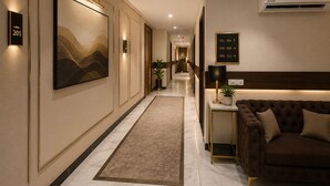 A hotel hallway with a modern design, including a large framed artwork, a potted plant, a sofa, and a sign indicating room numbers. - Qotel Comfort Oasis Rajouri Garden (New Delhi)